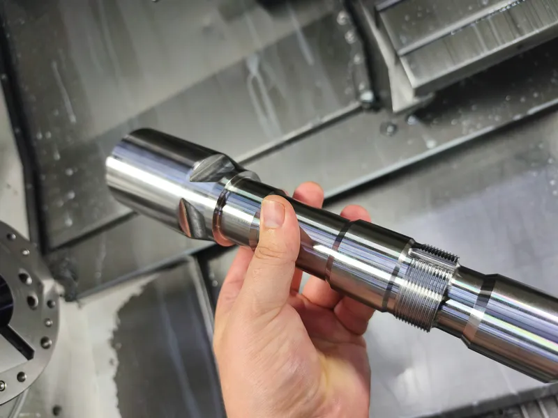 Gedrehte Welle mit Absätzen und Gewinde in der Hand vor der Maschine